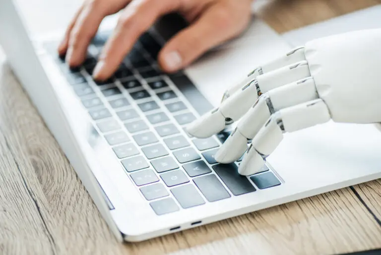 Menschliche Hand und Roboterhand tippen gemeinsam auf einer Laptop-Tastatur